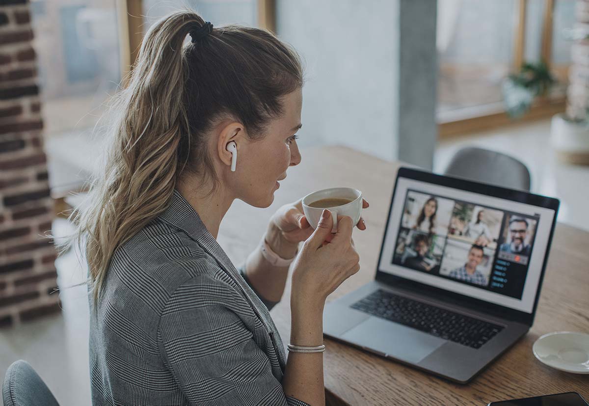 Frau mit Kaffeetasse in der Hand sitzt vor dem Laptop