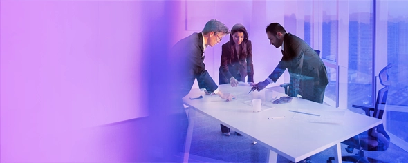 3 Personen stehen um einen Tisch herum und deuten auf ein Dokument